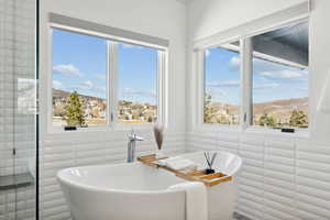 Bathroom with a tub, a healthy amount of sunlight, and tile walls