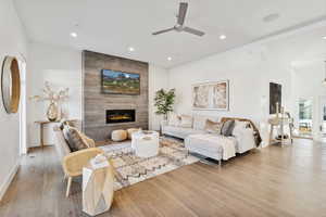 Living room with a large fireplace, light hardwood / wood-style floors, and ceiling fan