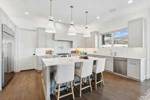 Kitchen featuring pendant lighting, a center island, decorative backsplash, appliances with stainless steel finishes, and dark hardwood / wood-style flooring