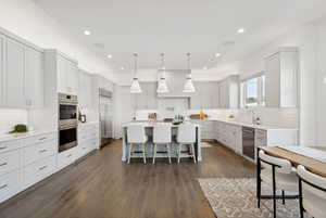 Kitchen with dark hardwood / wood-style flooring, a breakfast bar, stainless steel appliances, pendant lighting, and a kitchen island