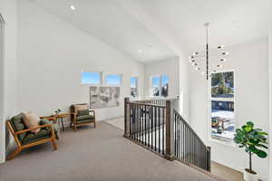 Hall featuring carpet flooring, high vaulted ceiling, and a chandelier