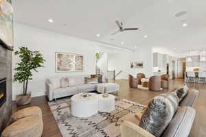 Living room with wood-type flooring, a large fireplace, and ceiling fan