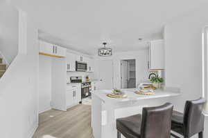 Kitchen with kitchen peninsula, decorative light fixtures, light hardwood / wood-style floors, white cabinetry, and stainless steel appliances