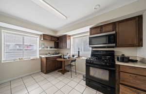 Kitchen featuring a healthy amount of sunlight, black range with gas stovetop, light tile patterned floors, and dark brown cabinetry