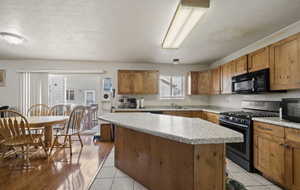 Kitchen with black appliances, light hardwood / wood-style floors, a kitchen island, and a textured ceiling