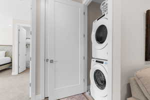 Laundry area featuring light colored carpet and stacked washing maching and dryer