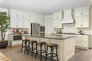 Kitchen with a center island with sink, sink, dark hardwood / wood-style floors, custom range hood, and stainless steel appliances