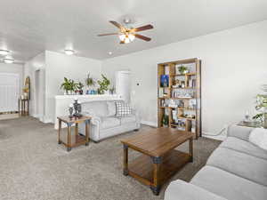 Carpeted living room featuring ceiling fan and a textured ceiling