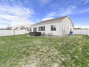 Rear view of property with a mountain view, a yard, and a hot tub