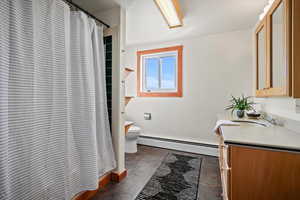 Bathroom with a shower with shower curtain, vanity, toilet, and a baseboard heating unit