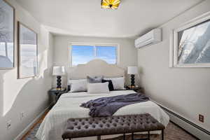 Bedroom with an AC wall unit and a baseboard heating unit