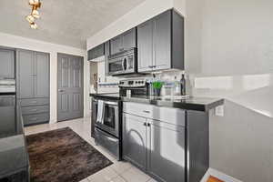 Kitchen featuring decorative backsplash, appliances with stainless steel finishes, light tile patterned floors, and gray cabinetry