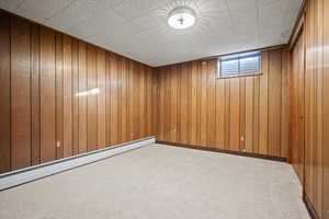 Basement featuring wood walls, light carpet, and a baseboard heating unit