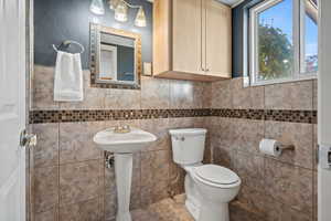 Bathroom featuring tile patterned floors, sink, toilet, and tile walls