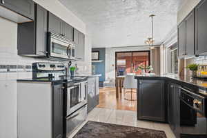 Kitchen featuring appliances with stainless steel finishes, a textured ceiling, tasteful backsplash, and light tile patterned floors