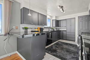 Kitchen featuring dishwasher, backsplash, pendant lighting, gray cabinets, and light tile patterned flooring