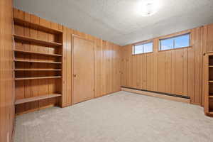 Basement featuring light carpet, a baseboard radiator, and wooden walls