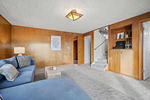 Carpeted living room with built in features and wooden walls