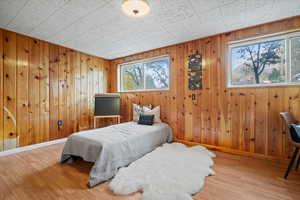 Bedroom with multiple windows, wooden walls, and light wood-type flooring