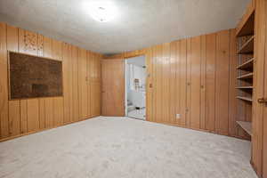 Empty room featuring a textured ceiling, light colored carpet, and wooden walls