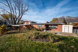 Back of property with a lawn, a mountain view, and a carport