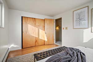 Bedroom featuring hardwood / wood-style floors, a closet, and a baseboard heating unit