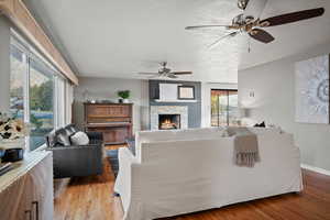 Living room with hardwood / wood-style floors, ceiling fan, and a tiled fireplace