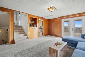 Living room featuring carpet flooring, french doors, built in features, and wooden walls