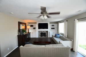 Living room featuring ceiling fan, a stone fireplace, and dark wood-type flooring