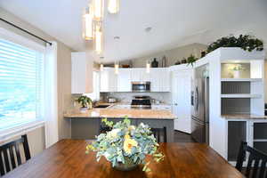 Kitchen featuring white cabinetry, light stone countertops, stainless steel appliances, and hanging light fixtures