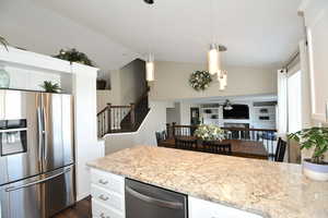 Kitchen with lofted ceiling, stainless steel fridge with ice dispenser, light stone countertops, decorative light fixtures, and white cabinetry