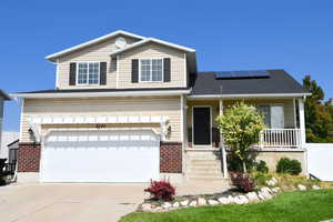 View of front of home featuring covered porch, a garage, and solar panels