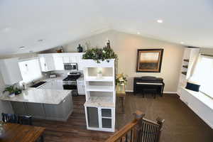 Kitchen with kitchen peninsula, appliances with stainless steel finishes, vaulted ceiling, pendant lighting, and white cabinets