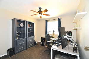 Office area with ceiling fan and dark colored carpet