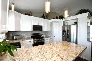 Kitchen featuring stainless steel appliances, white cabinetry, and hanging light fixtures