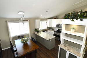 Kitchen with sink, vaulted ceiling, decorative light fixtures, white cabinetry, and stainless steel appliances