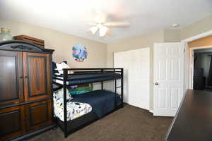 Bedroom with ceiling fan, a textured ceiling, and dark colored carpet