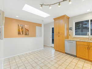 Kitchen featuring a skylight, light stone counters, stainless steel dishwasher, sink, and light tile patterned flooring