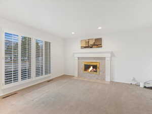 Unfurnished living room featuring a tile fireplace and light colored carpet