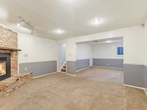 Basement with light carpet, a textured ceiling, track lighting, and a fireplace