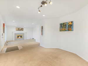 Unfurnished living room with carpet flooring, rail lighting, and a tile fireplace