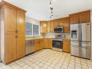 Kitchen featuring sink, tasteful backsplash, light stone counters, light tile patterned floors, and appliances with stainless steel finishes