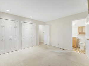 Unfurnished bedroom featuring light carpet, two closets, and ensuite bathroom