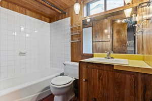 Full bathroom featuring wooden walls, vanity, toilet, and tiled shower / bath combo