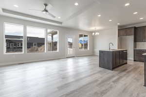 Kitchen featuring dark brown cabinetry, sink, light hardwood / wood-style floors, a center island with sink, and ceiling fan with notable chandelier