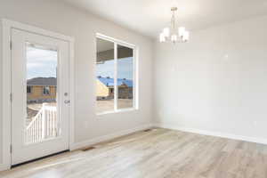 Unfurnished dining area with light wood-type flooring, an inviting chandelier, and a healthy amount of sunlight