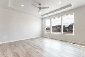 Spare room featuring light hardwood / wood-style floors, a raised ceiling, and ceiling fan