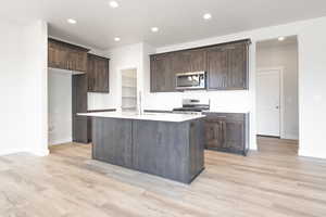 Kitchen with dark brown cabinetry, stainless steel appliances, a kitchen island with sink, sink, and light hardwood / wood-style floors