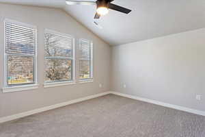 Empty room featuring carpet flooring, ceiling fan, and vaulted ceiling