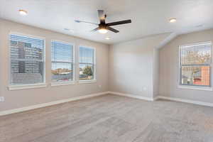 Carpeted empty room with ceiling fan, a textured ceiling, and a wealth of natural light